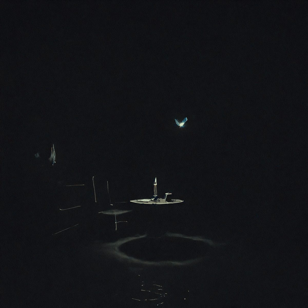 The primary subject of the image is a lit candle on a table. The setting is a dark room, and the visual style appears to be a photo. The dominant colors are black and white, creating a moody atmosphere.